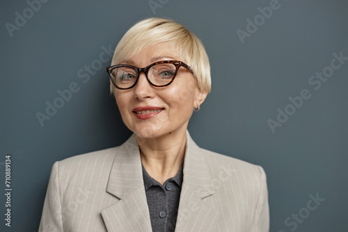 Close up portrait of elegant mature woman wearing glasses and looking at camera with smile against grey background