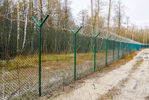 A green metal mesh fence with coiled barbed wire around the restricted area of a military facility