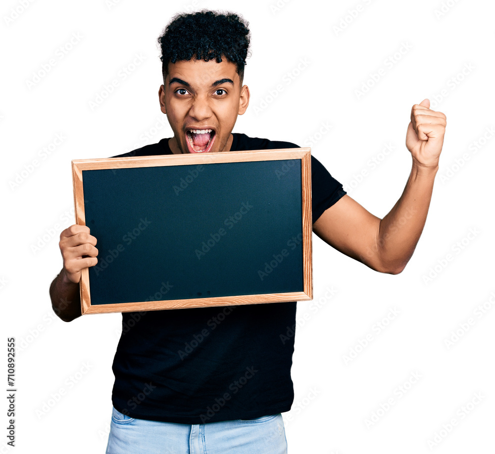 Young african american man holding blackboard screaming proud, celebrating victory and success very excited with raised arms Young african american man holding blackboard screaming proud, celebrating victory and success very excited with raised arms
