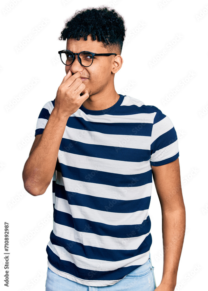 Young african american man wearing casual clothes and glasses smelling something stinky and disgusting, intolerable smell, holding breath with fingers on nose. bad smell Young african american man wearing casual clothes and glasses smelling something stinky and disgusting, intolerable smell, holding breath with fingers on nose. bad smell