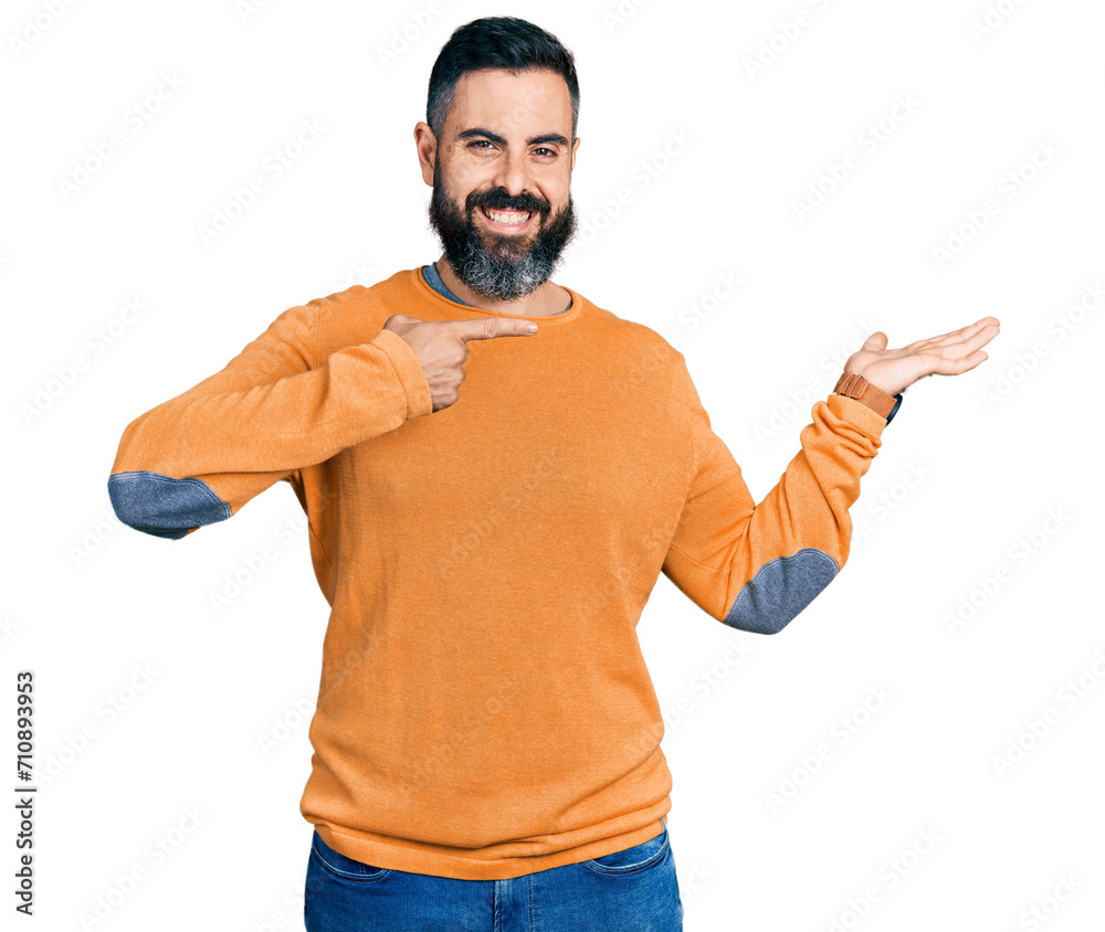 Hispanic man with beard wearing casual winter sweater amazed and smiling to the camera while presenting with hand and pointing with finger.