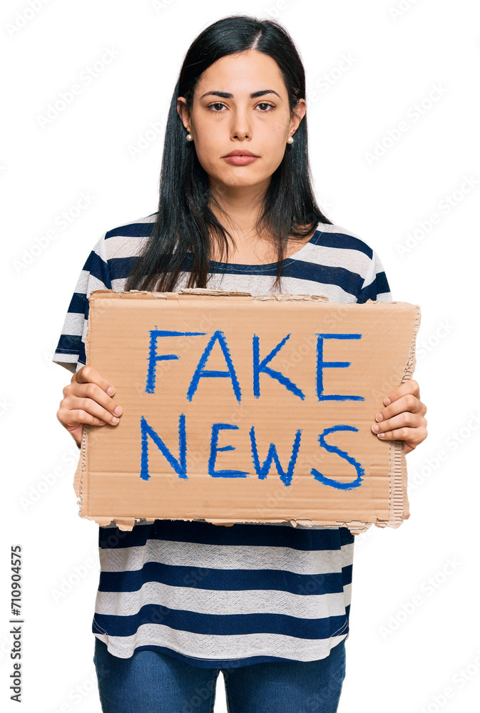 Beautiful young woman holding fake news banner thinking attitude and sober expression looking self confident Beautiful young woman holding fake news banner thinking attitude and sober expression looking self confident