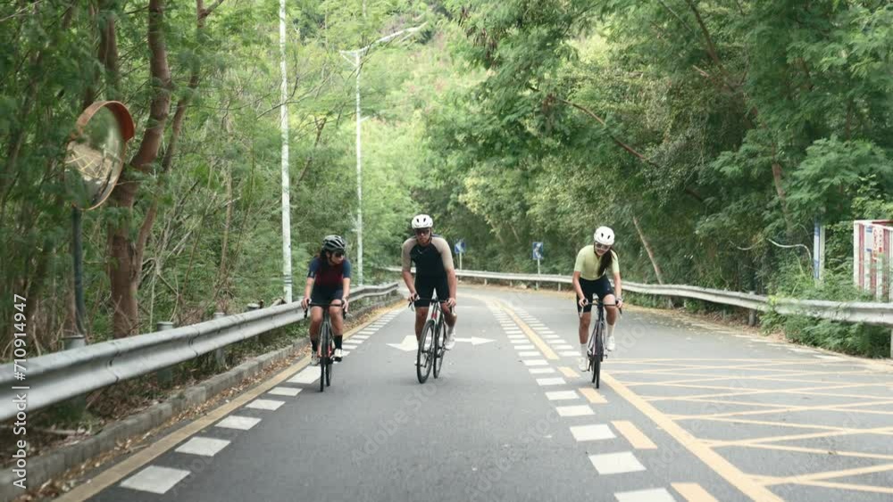 three young asian adults chatting while cycling on uphill rural road three young asian adults chatting while cycling on uphill rural road