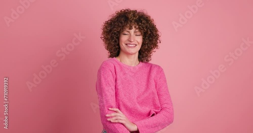 Smiling standing young curly haired woman on pink background photo
