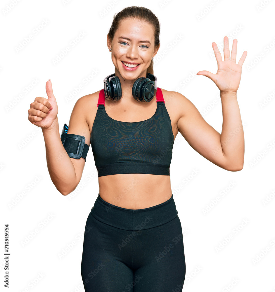 Beautiful blonde woman wearing gym clothes and using headphones showing and pointing up with fingers number six while smiling confident and happy. Beautiful blonde woman wearing gym clothes and using headphones showing and pointing up with fingers number six while smiling confident and happy.