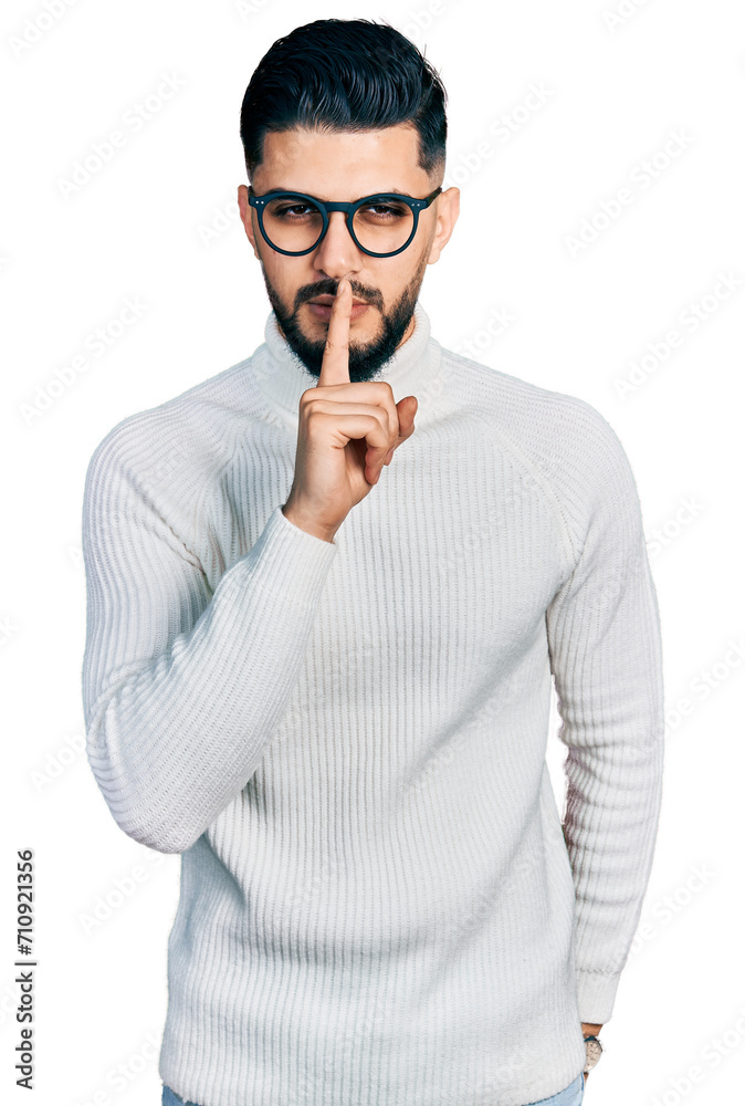 Young arab man with beard wearing elegant turtleneck sweater and glasses asking to be quiet with finger on lips. silence and secret concept. Young arab man with beard wearing elegant turtleneck sweater and glasses asking to be quiet with finger on lips. silence and secret concept.