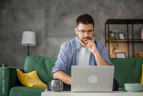 One adult man sitting in the living room at home and working on laptop, modern business concept, working from home  photo