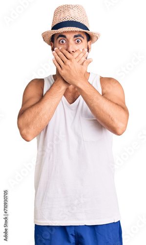 Young hispanic man wearing casual summer hat shocked covering mouth with hands for mistake. secret concept.