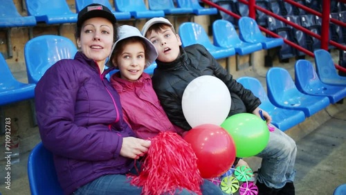 Mother, daughter and son with balloons sit on seats at stadium photo