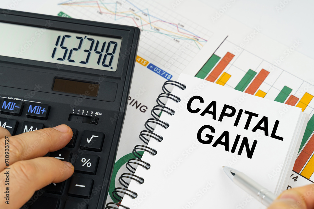 On the table there is a calculator, reports with graphs and a notepad with the inscription - capital gain On the table there is a calculator, reports with graphs and a notepad with the inscription - capital gain