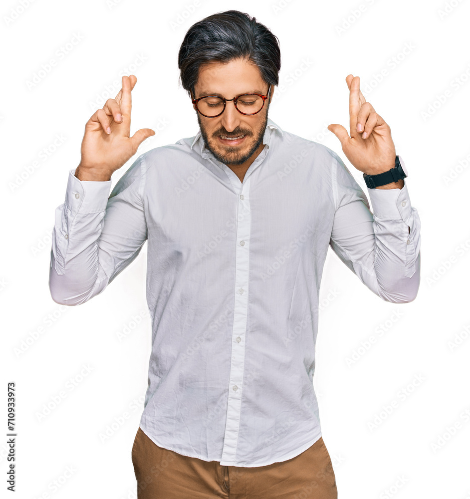 Naklejka premium Young hispanic man wearing business shirt and glasses gesturing finger crossed smiling with hope and eyes closed. luck and superstitious concept.