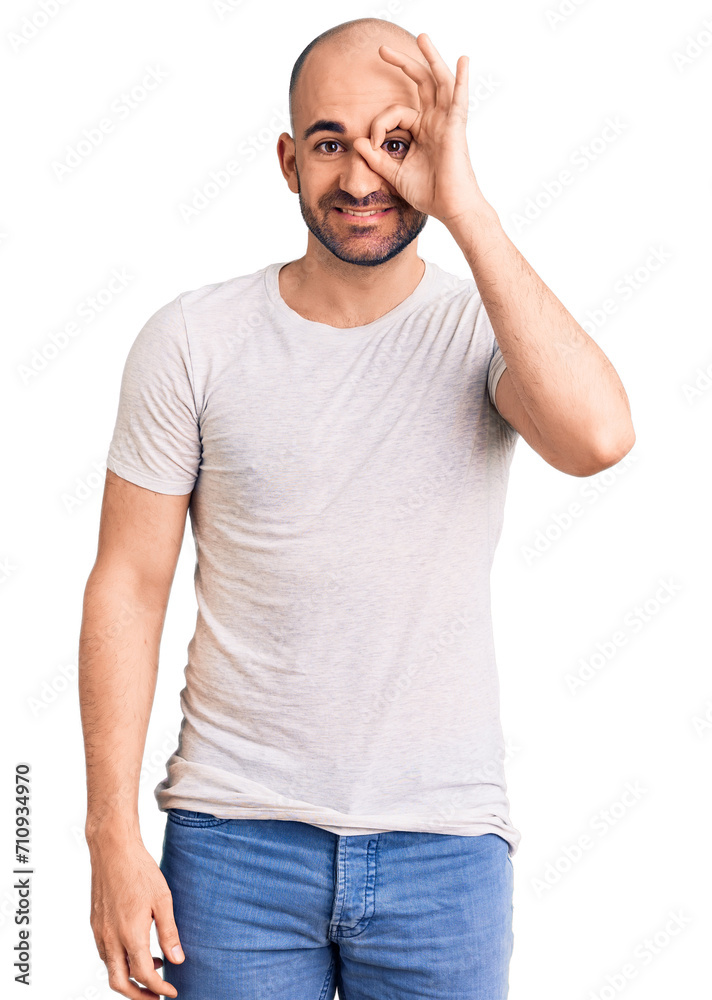 Young handsome man wearing casual t shirt doing ok gesture with hand smiling, eye looking through fingers with happy face.