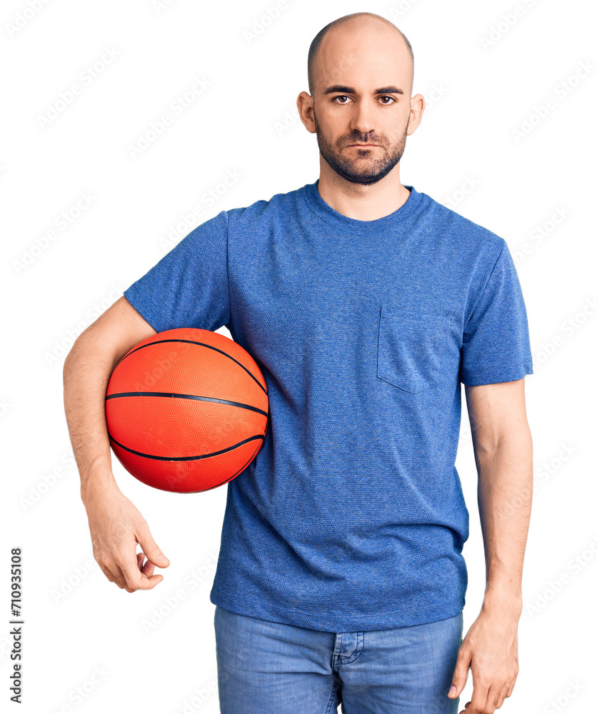 Young handsome man holding basketball ball thinking attitude and sober expression looking self confident Young handsome man holding basketball ball thinking attitude and sober expression looking self confident