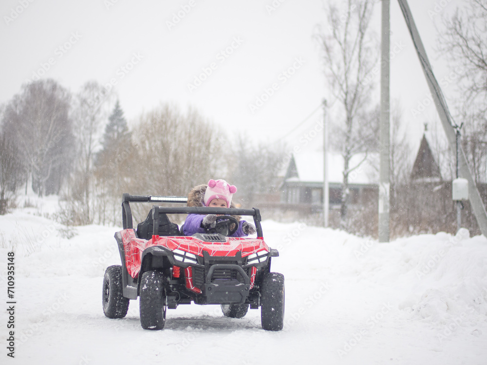 girl drives an electric toy car in winter on the street. Street toys. Children in a car with a battery. girl drives an electric toy car in winter on the street. Street toys. Children in a car with a battery.