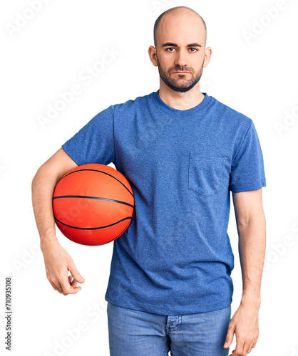 Young handsome man holding basketball ball thinking attitude and sober expression looking self confident