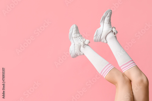 Legs of young woman in stylish white sneakers on pink background