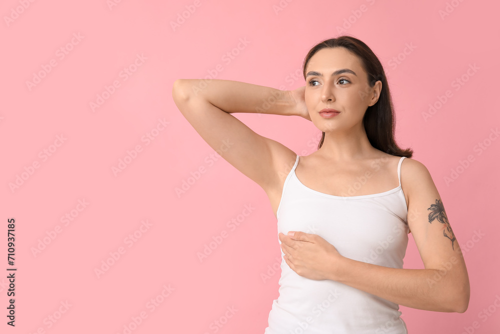 Young woman checking her breast on pink background. Cancer awareness concept Young woman checking her breast on pink background. Cancer awareness concept