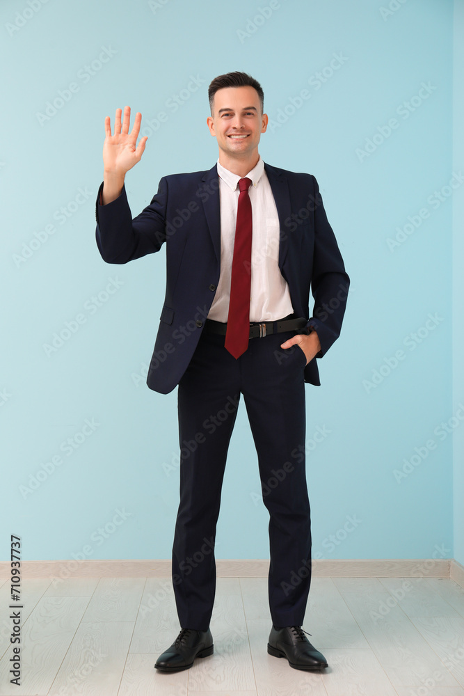 Handsome businessman waving hand near blue wall Handsome businessman waving hand near blue wall