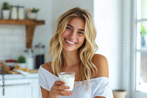 Cheerful woman enjoying yogurt in home kitchen, smiling at camera. photo