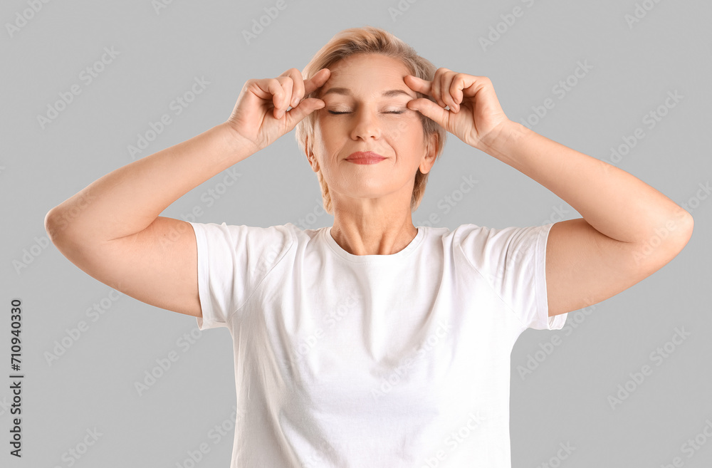 Mature woman doing face building exercise on light background Mature woman doing face building exercise on light background
