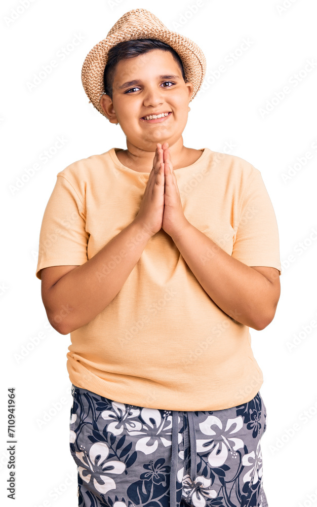 Little boy kid wearing summer hat and hawaiian swimsuit praying with hands together asking for forgiveness smiling confident. Little boy kid wearing summer hat and hawaiian swimsuit praying with hands together asking for forgiveness smiling confident.