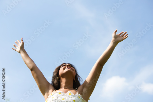 Beautiful Spanish brunette woman with long curly hair raises her arms to the blue sky. The woman is happy and thanks god and life for every day. Concept happiness and thankfulness. photo