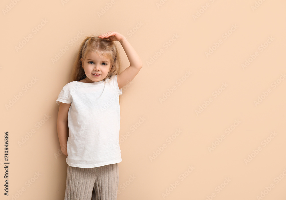Cute little girl measuring height on beige background Cute little girl measuring height on beige background