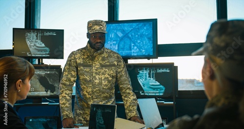 African American naval general coming in office for conference and talking to Caucasian women about marine dislocation. Planning of militarian operation at army staff meeting. photo