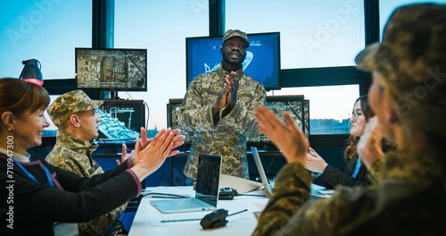 African American man, young head in army finishing military conference at office with screens and staff applauding to speakers. Multiethnic male and female staff of troops at meeting. photo