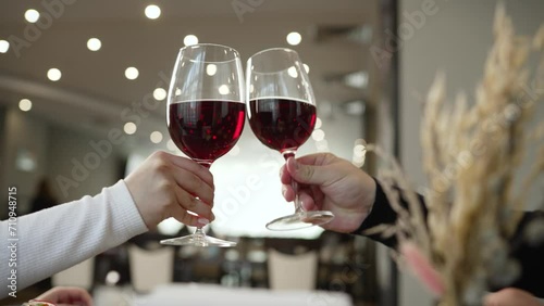 A family raises a toast at the dinner table in a restaurant. Young happy couple on a romantic date. A guy and a girl on a date in a restaurant raise glasses of red wine, close-up. photo