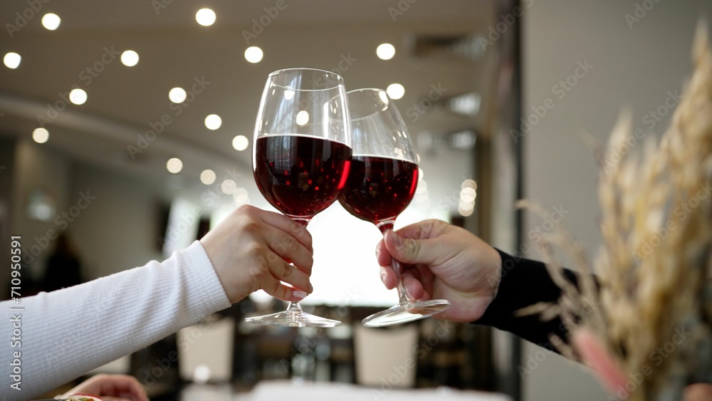 A family raises a toast at the dinner table in a restaurant. Young happy couple on a romantic date. A guy and a girl on a date in a restaurant raise glasses of red wine, close-up.
