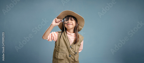 A little girl is wearing a camping clothes, holding a magnifying glass for studying.