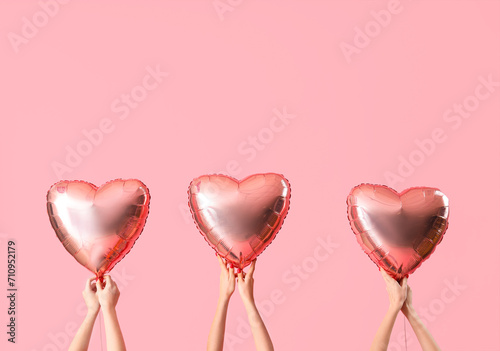 Female hands holding heart-shaped balloons on pink background. Valentine's Day celebration photo
