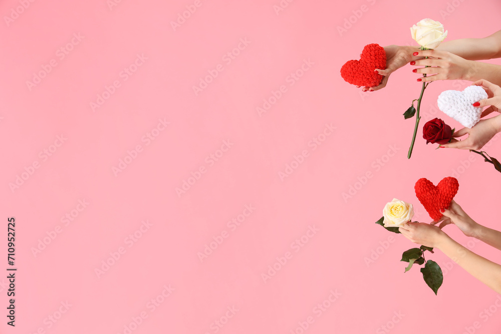 Female hands holding knitted hearts and roses on pink background. Valentine's Day celebration