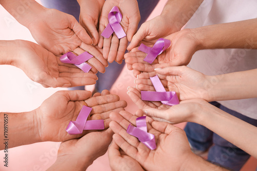 People with lavender awareness ribbons on pink background, closeup. World Cancer Day