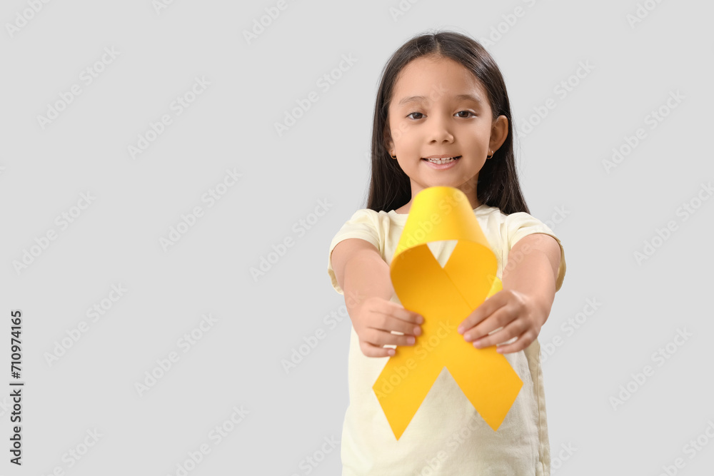 Cute little Asian girl with yellow ribbon on grey background. Childhood cancer awareness concept Cute little Asian girl with yellow ribbon on grey background. Childhood cancer awareness concept