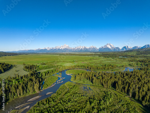 aerial view of winding river, green forest and snow mountain range outside Grand Teton national park