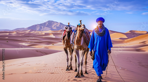 Camel rider with camels travelling over dunes in the desert