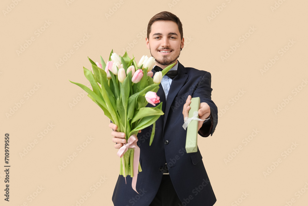 Young man with bouquet of beautiful tulips and gift box on beige background. International Women's Day Young man with bouquet of beautiful tulips and gift box on beige background. International Women's Day