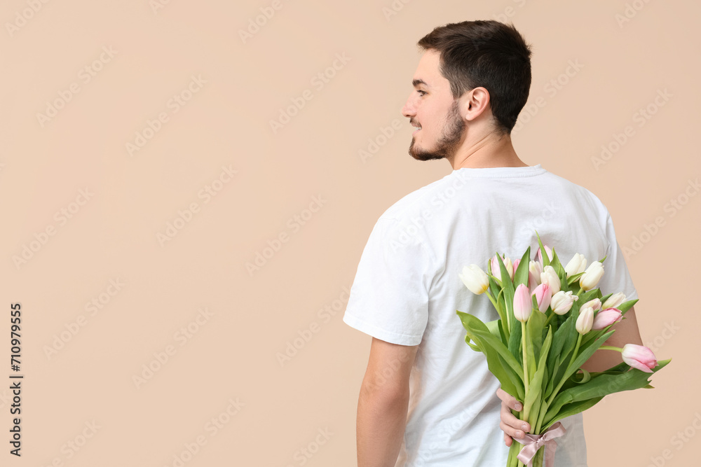 Young man with bouquet of beautiful tulips on beige background. International Women's Day