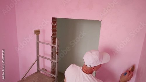 Worker in cap and white clothes paints wall in room photo