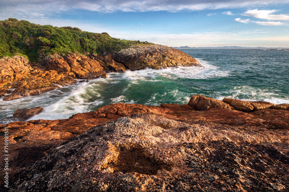 Waves on red rocks alongside ocean at broughton island near Hawks Nest in NSW Australia