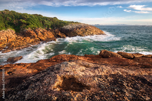 Waves on red rocks alongside ocean at broughton island near Hawks Nest in NSW Australia