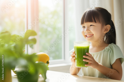 Little kid girl of asian appearance holding a glass of green juice, smoothie, children's health in her hands