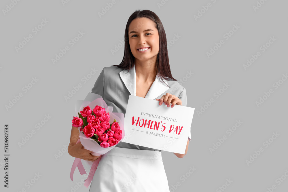 Young chambermaid with bouquet of tulips and greeting card on light background. International Women's Day