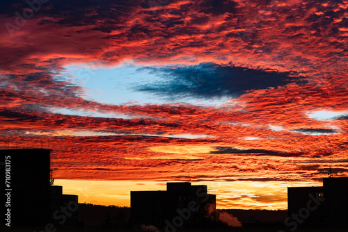 Beautiful sunset with fallstreak hole in red fiery sky and a buildings silhouette. Majestic orange clouds with large blue gap at winter dusk. Miracle open heaven in scenic skyline of Czech city Tabor.