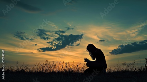 Silhouette of woman kneeling down praying for worship God at sky background. Christians pray to jesus christ for calmness. In morning people got to a quiet place and prayed. copy space photo