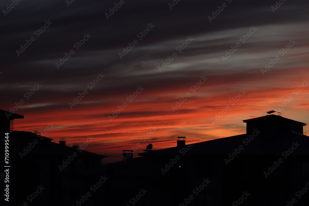 A dramatic sunset with radiant hues of orange and red streaking across the sky, silhouetting the rooftops of urban buildings. A dramatic sunset with radiant hues of orange and red streaking across the sky, silhouetting the rooftops of urban buildings.
