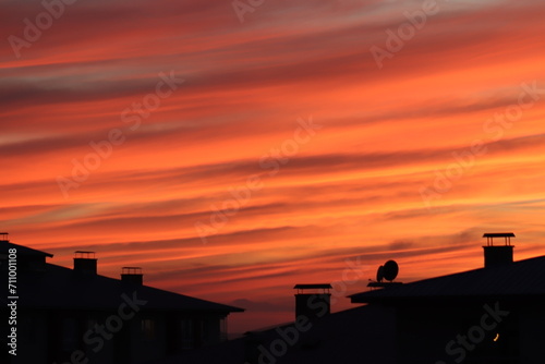 A dramatic sunset with radiant hues of orange and red streaking across the sky, silhouetting the rooftops of urban buildings. photo
