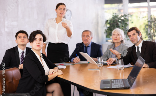 Focused interested young Hispanic businesswoman sitting at table in office, listening attentively to presentation of partners during business meeting